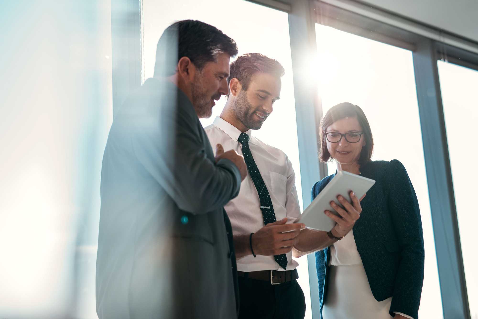 three people standing clustered around a paper, gray, black